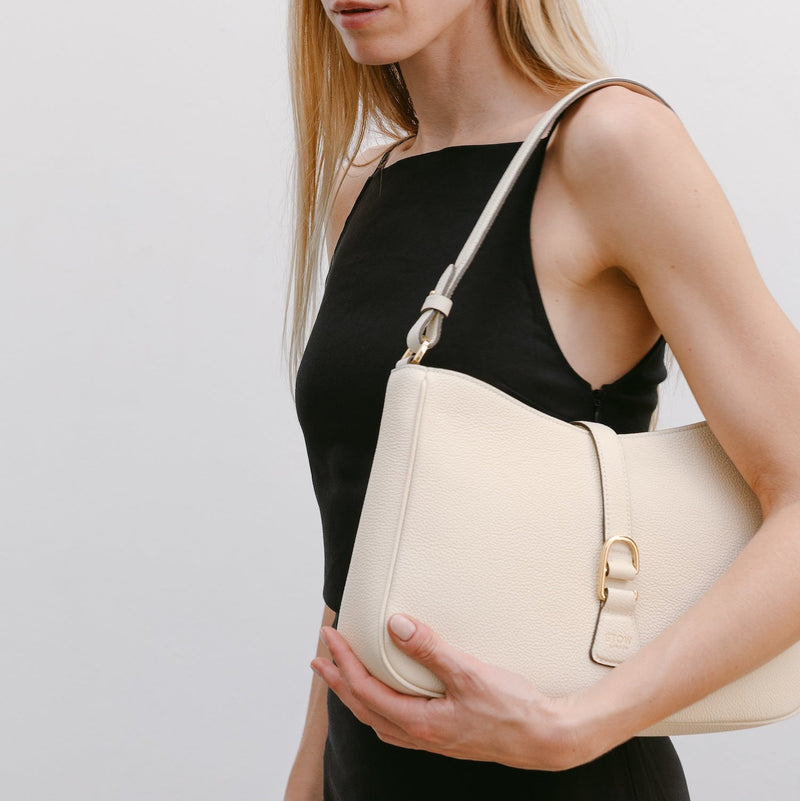 Model wearing STOW London's Beth Shoulder bag in Spring Moon pebbled leather on her shoulder featuring gold-coated stainless steel hardware and clip on a white background