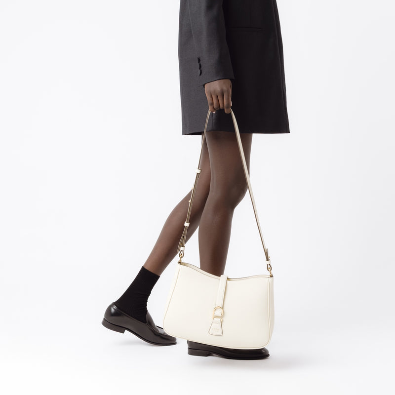 Model holding STOW London's Beth bag and detachable crossbody strap in Spring Moon leather featuring gold stainless steel hardware on a white background
