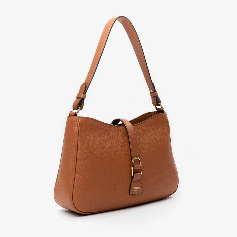 Off-axis view of STOW London's Beth bag in Earth Tan pebbled and smooth leather featuring gold-coated stainless steel hardware and clip on a white background