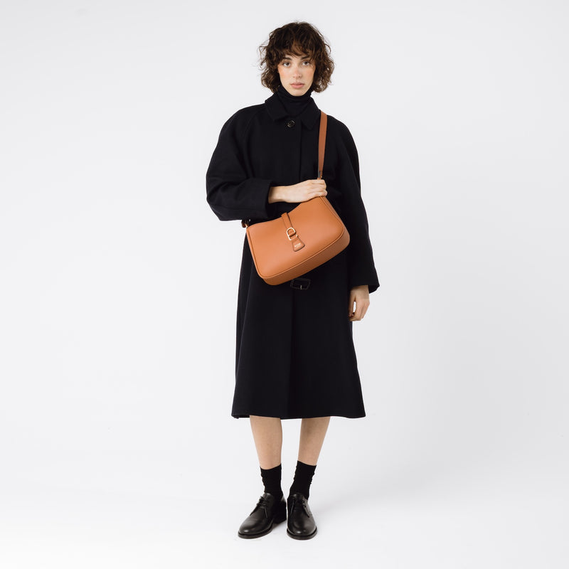 STOW London's Earth Tan Beth bag worn crossbody on model by its detachable leather strap featuring gold-coated stainless steel hardware on a white background