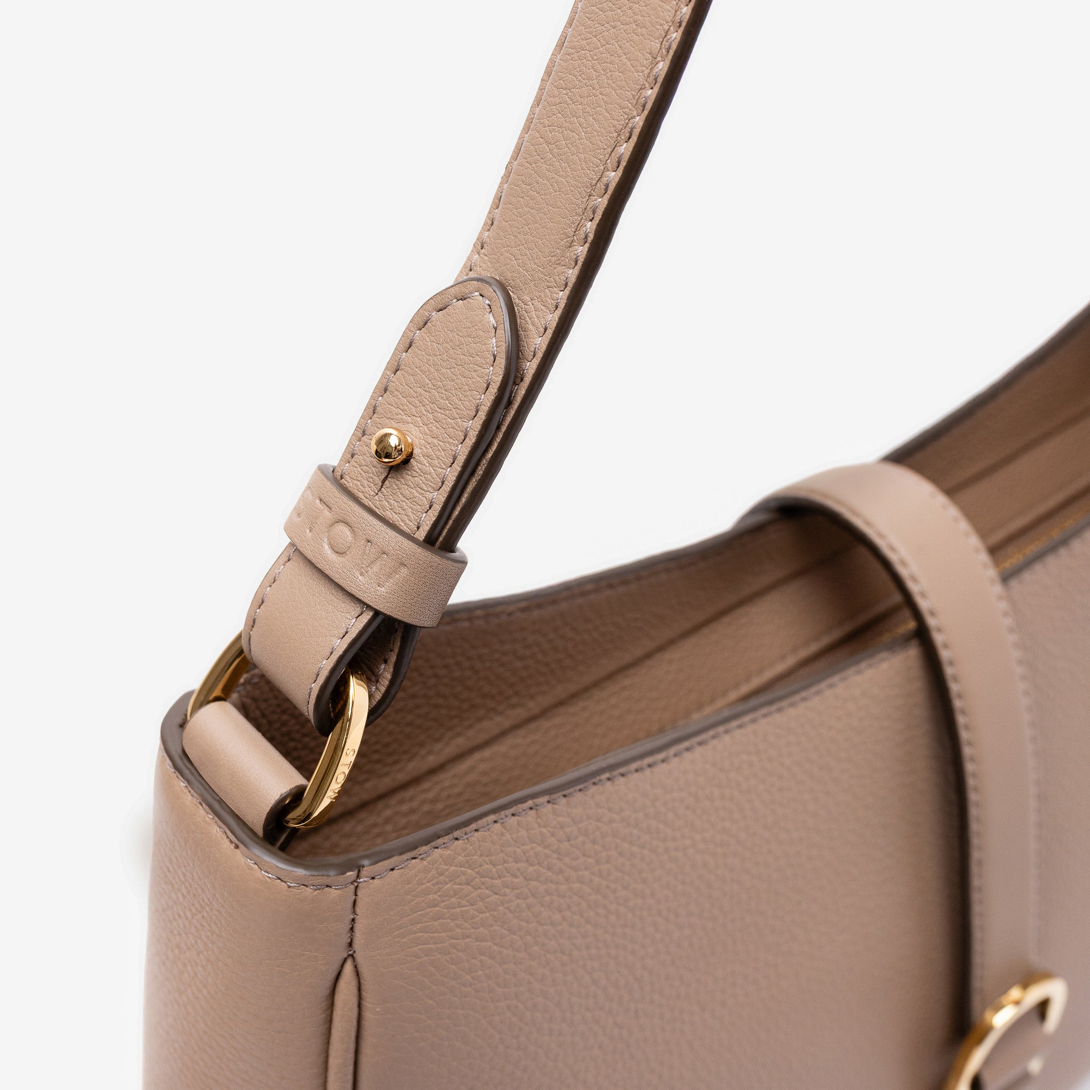 Close up shot of STOW London's Beth bag in Warm Taupe pebbled and smooth leather featuring the detachable strap and gold-coated, stainless steel hardware on a white background