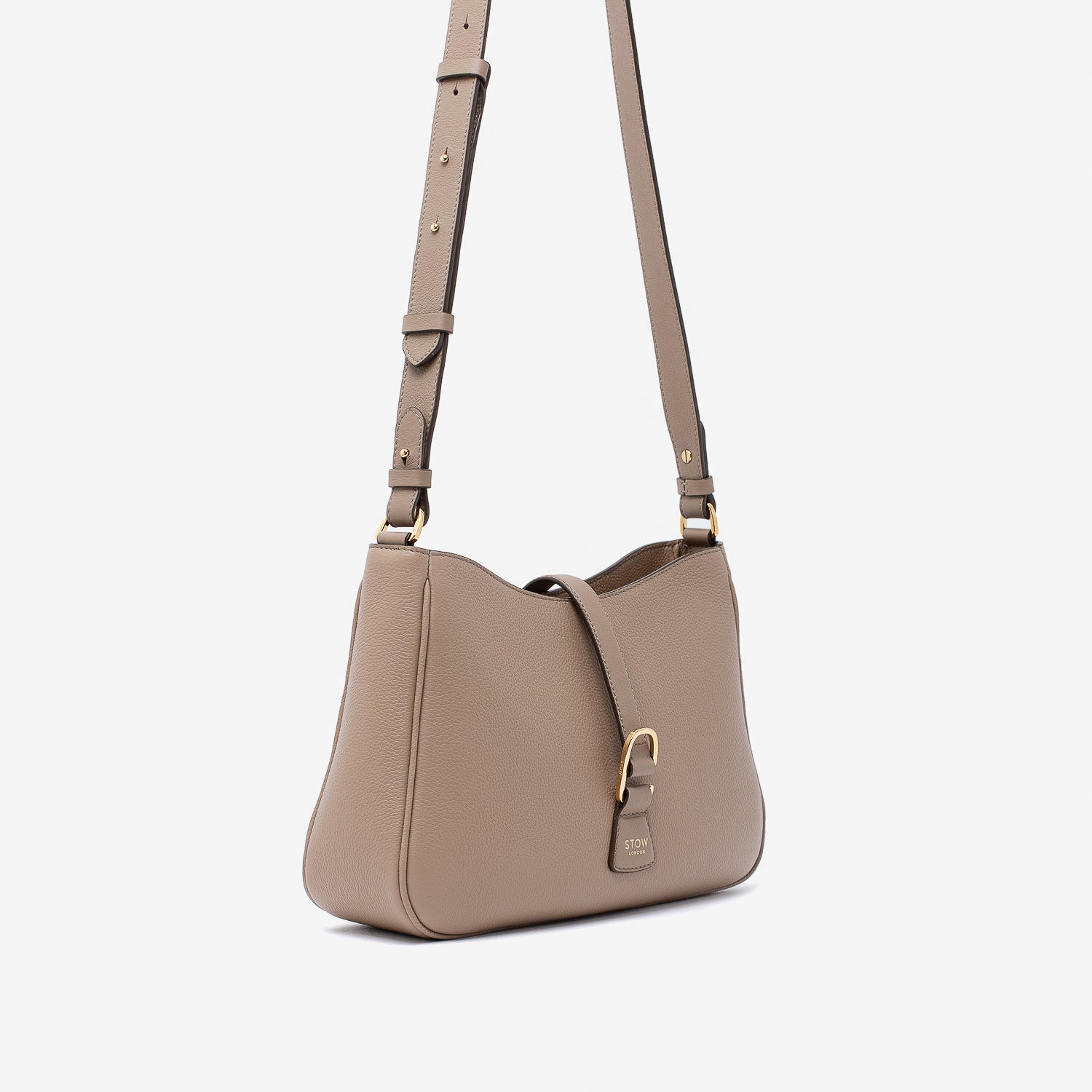 Off-axis view of STOW London's Beth bag and detachable crossbody strap in Warm Taupe leather featuring gold stainless steel hardware on a white background