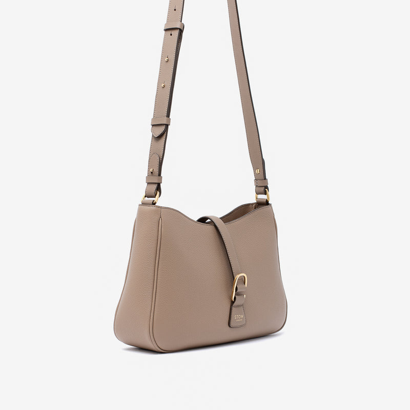 Off-axis view of STOW London's Beth bag and detachable crossbody strap in Warm Taupe leather featuring gold stainless steel hardware on a white background