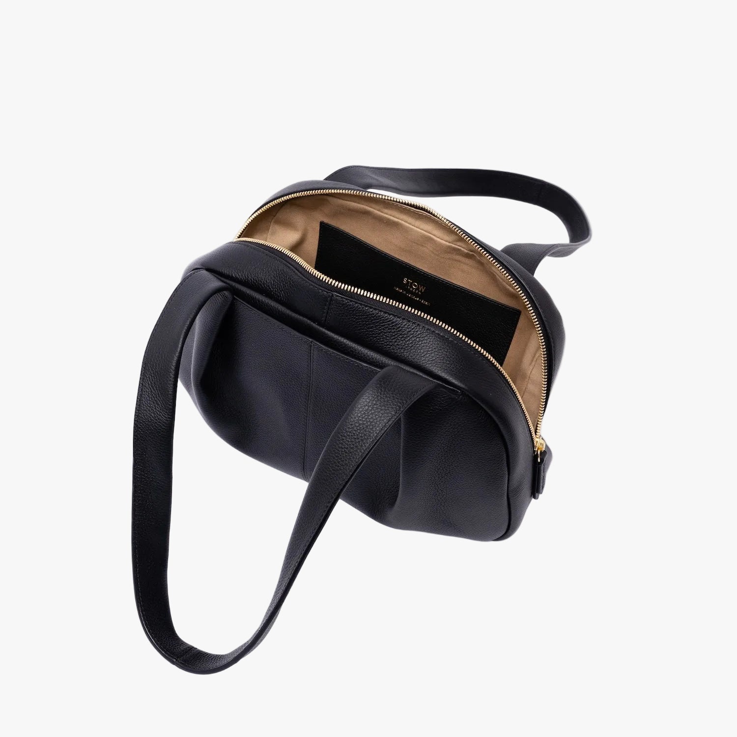 Top view of STOW London's Bowling bag in Black pebbled leather on a light grey background with the zip open showing the interior cotton lining and leather slip pocket 