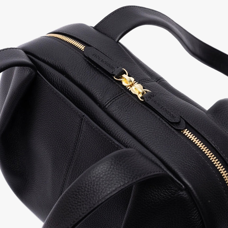Close up of shot of the gold zip closure of STOW London's Bowling bag in Black pebbled leather on a light grey background