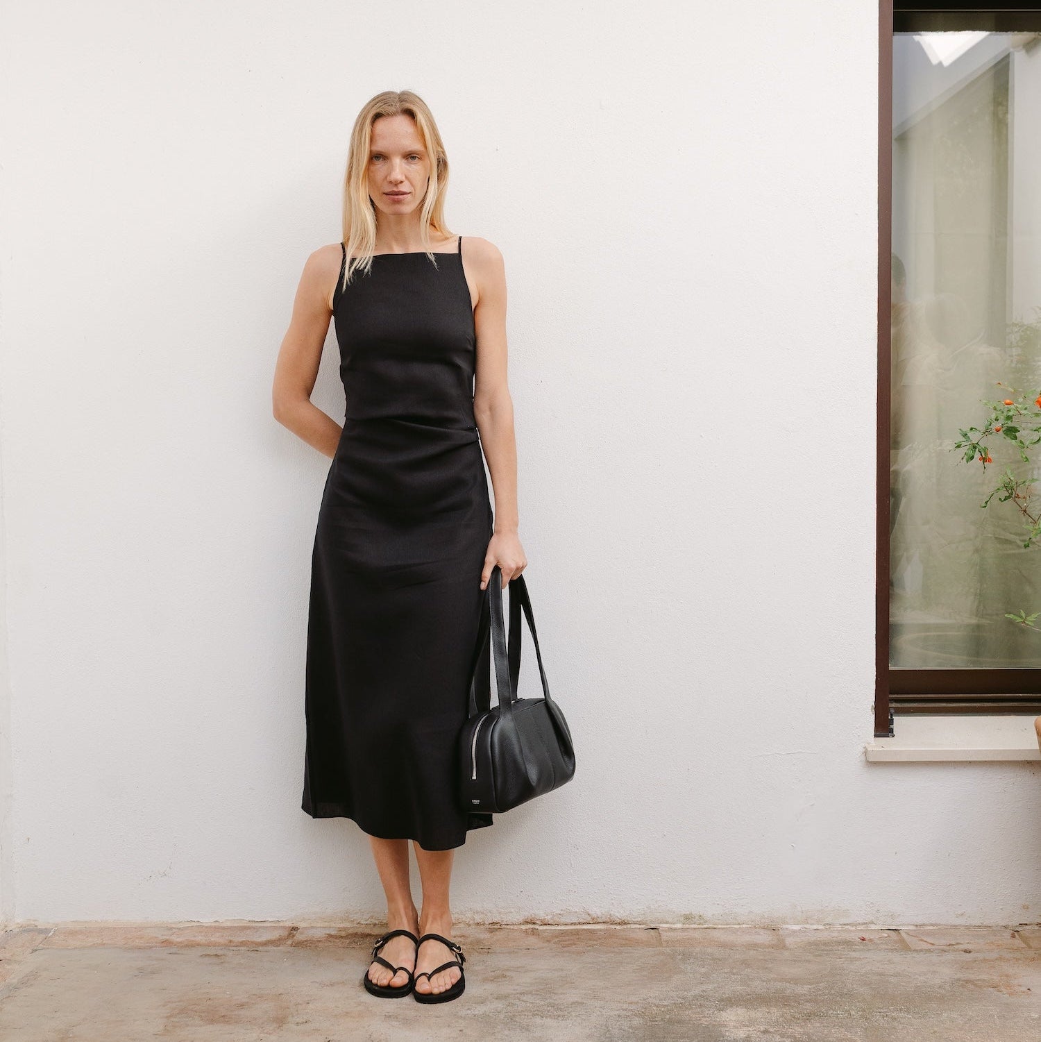 Model in black dress holding STOW London's Bowling bag in Black pebbled leather by the handles at her side featuring silver stainless steel hardware