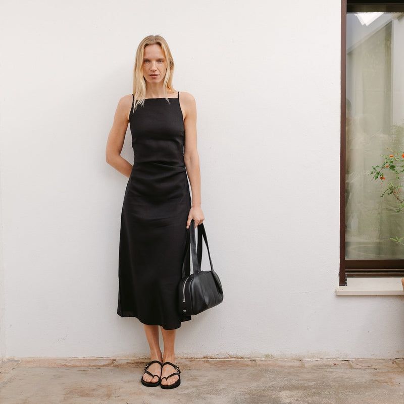 Model in black dress holding STOW London's Bowling bag in Black pebbled leather by the handles at her side featuring silver stainless steel hardware