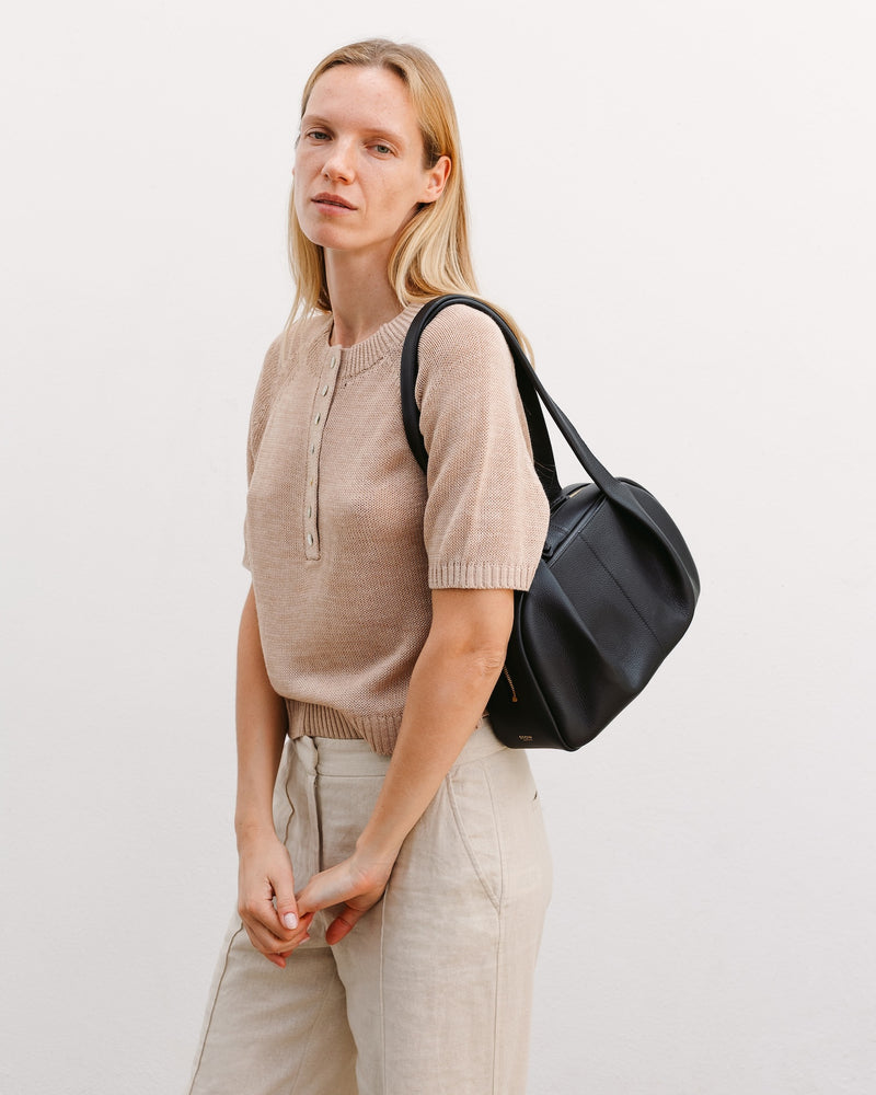 model wearing STOW London's Bowling bag in Black pebbled leather on her shoulder featuring the pleated front panel and gold-coated stainless steel hardware 