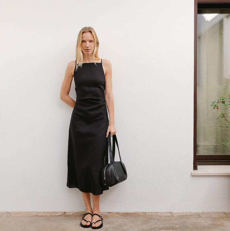 Model holding STOW London's Bowling bag in Black pebbled leather at her side featuring the pleated front panel and silver stainless steel hardware 