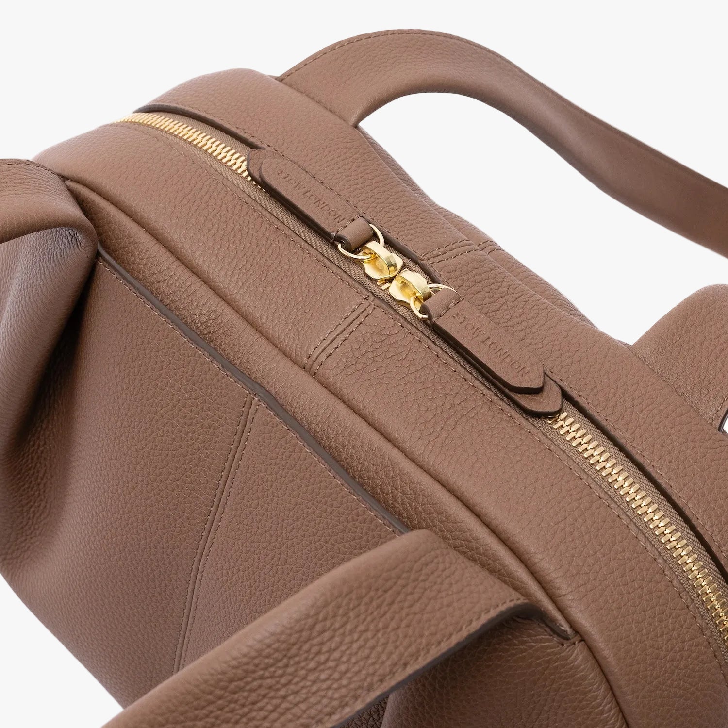 Close up of the zip top closure on STOW London's Bowling bag in Mocha pebbled leather featuring gold-coated stainless steel hardware on a light grey background