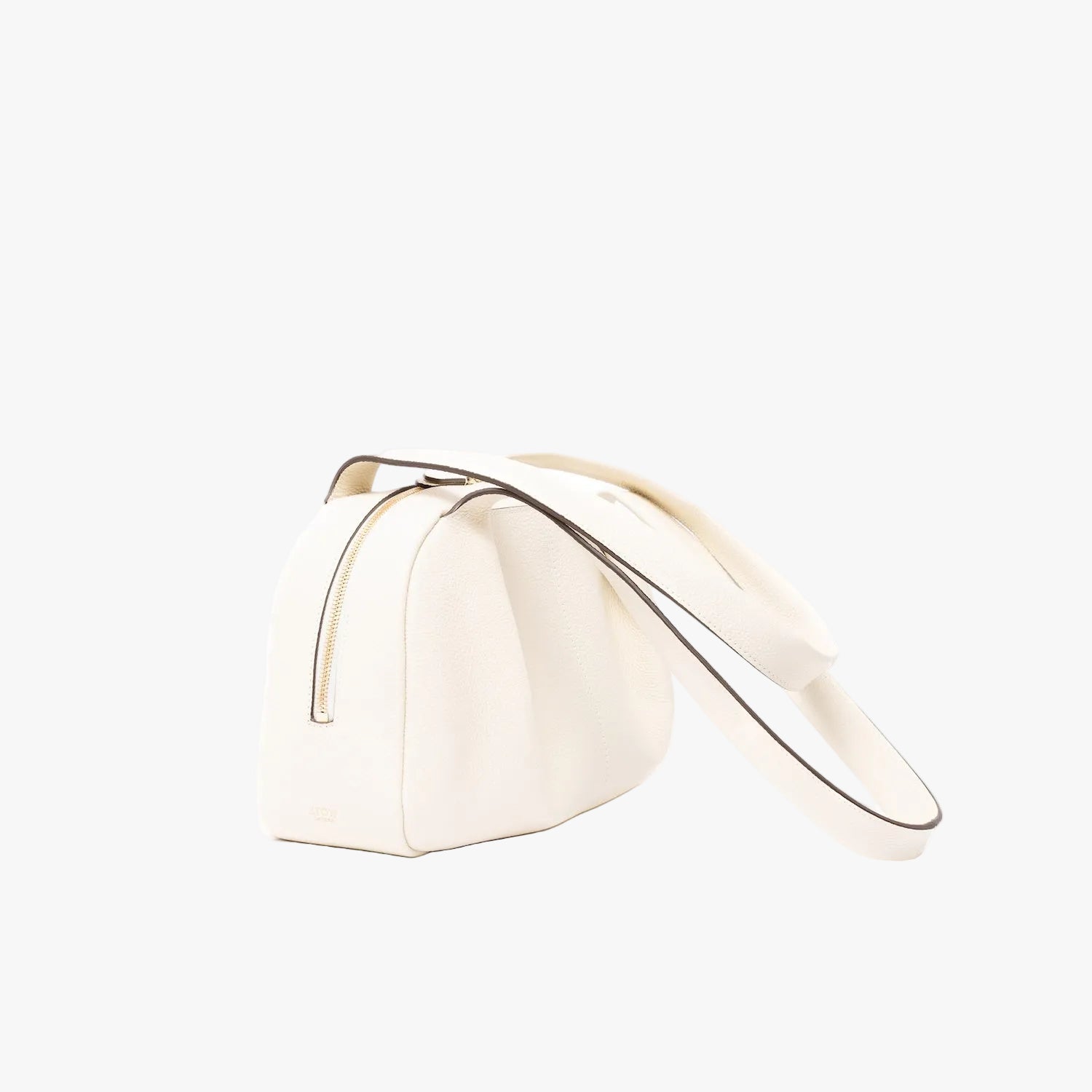 Off-axis view of STOW London's Bowling bag in Black pebbled leather featuring the pleated front panel and gold-coated stainless steel hardware on a light grey background