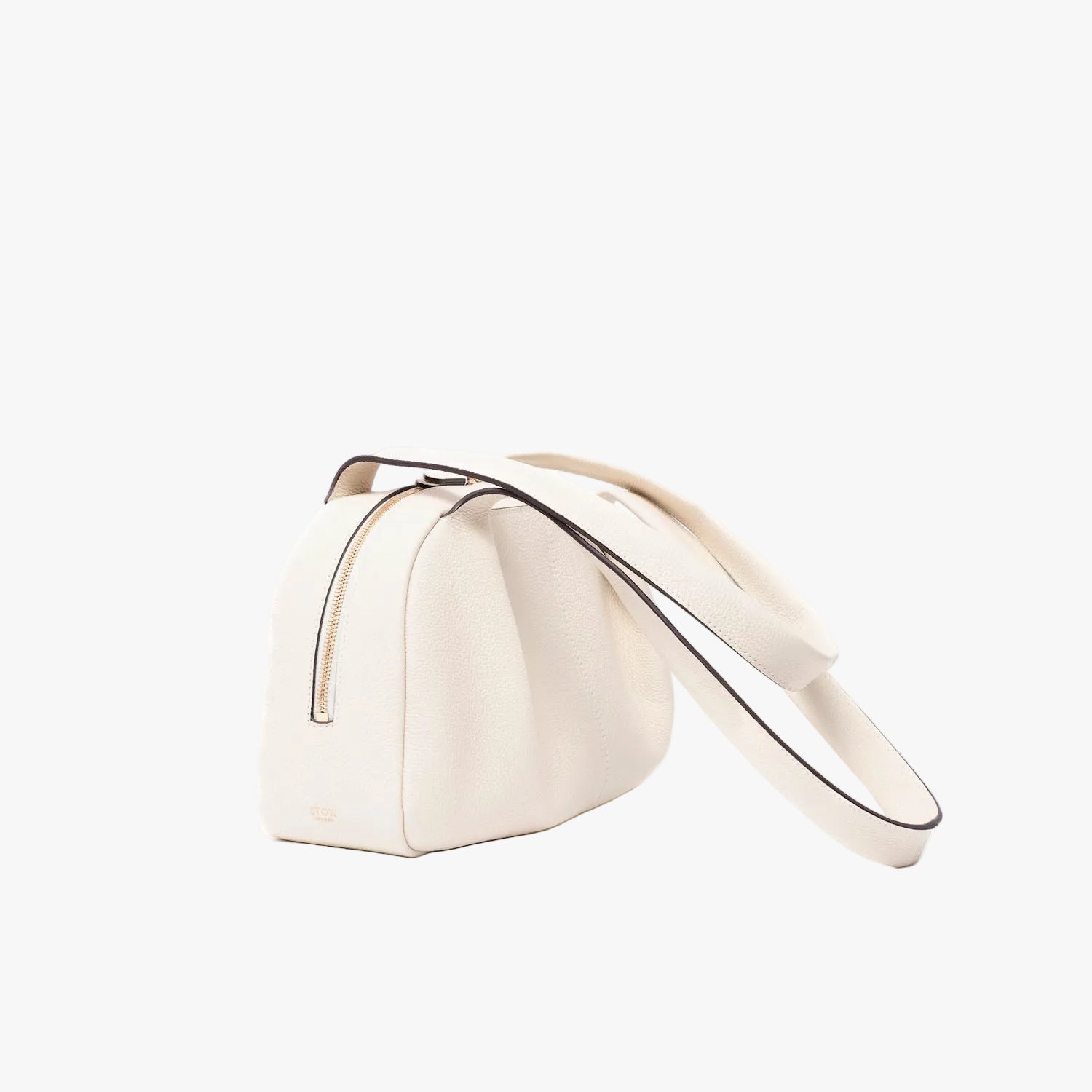 Off-axis view of STOW London's Bowling bag in Spring Moon pebbled leather featuring the pleated front panel and gold-coated stainless steel hardware on a light grey background