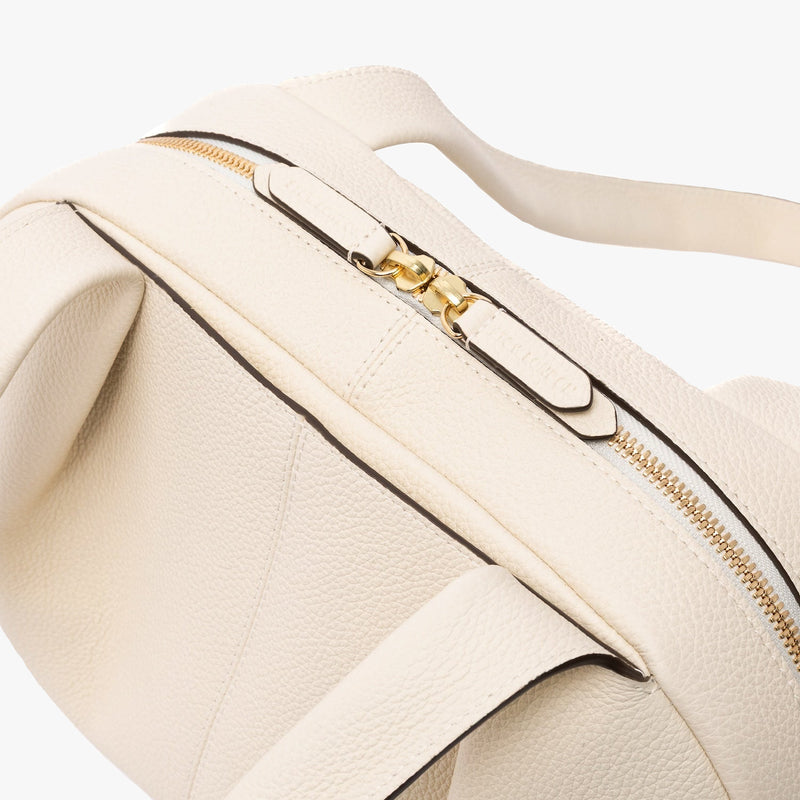 Close up of STOW London's Bowling bag in Spring Moon pebbled leather featuring the pleated front panel and the gold zip closure on a light grey background