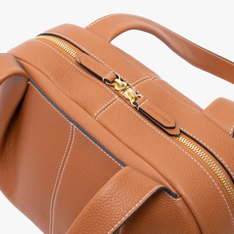 Close up of the zip top closure on STOW London's Bowling bag in Earth Tan pebbled leather featuring the front slip pocket and gold-coated stainless steel hardware on a light grey background