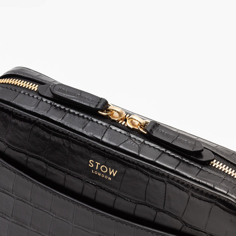 Close up of STOW London's Camera bag in Black Embossed Croc leather featuring gold-coated stainless steel hardware and brand engraved pull tabs on a white background
