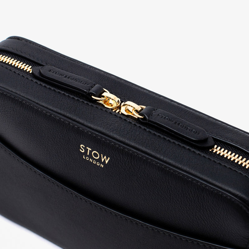 Close up of STOW London's Camera bag in Black Smooth leather featuring gold-coated stainless steel hardware and brand engraved pull tabs on a white background	
