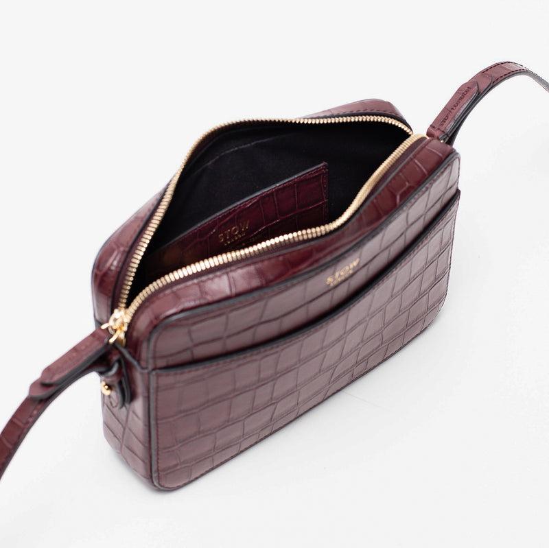 Top angled view of STOW London's Camera bag in Burgundy Embossed Croc leather with zipper open featuring gold-coated stainless steel hardware on a white background