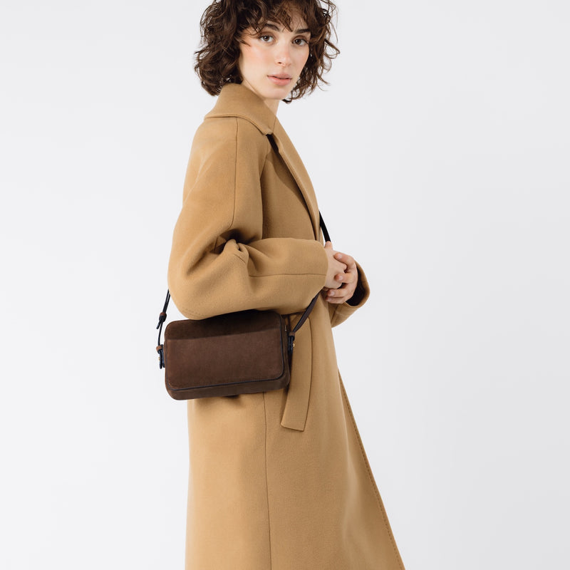 Model wearing STOW London's Camera bag in Chocolate Suede leather crossbody featuring gold-coated stainless steel hardware on a white background