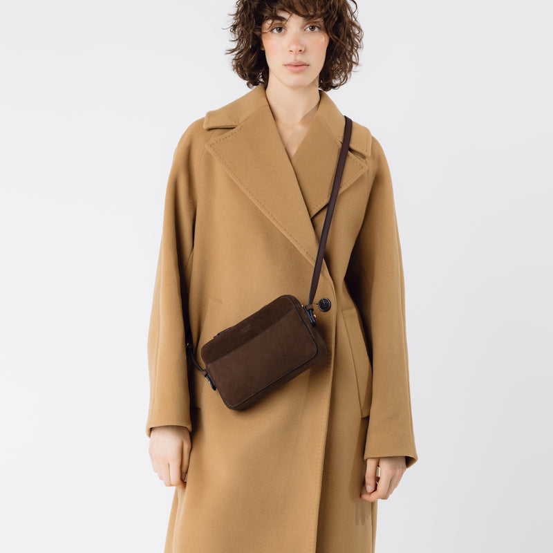 Model wearing STOW London's Camera bag in Chocolate Suede leather crossbody featuring gold-coated stainless steel hardware on a white background