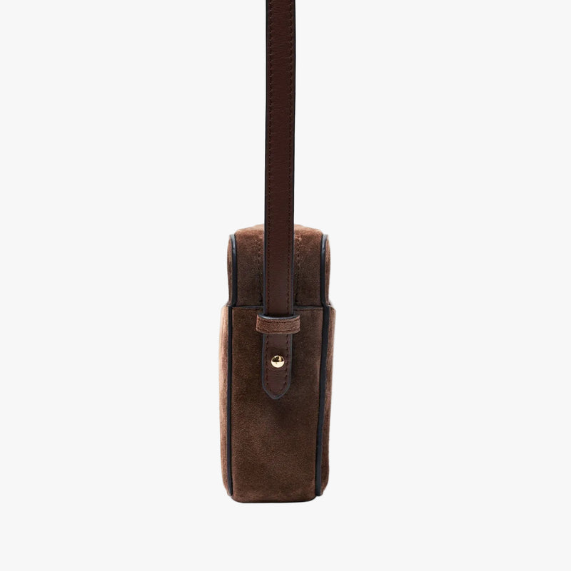 Side view of STOW London's Camera bag in Chocolate Suede leather with detachable crossbody strap featuring gold-coated stainless steel hardware on a light grey background