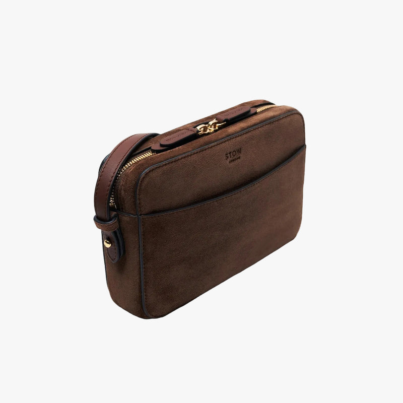 Off-axis view of STOW London's Camera bag in Chocolate Suede leather with detachable crossbody strap featuring gold-coated stainless steel hardware on a light grey background