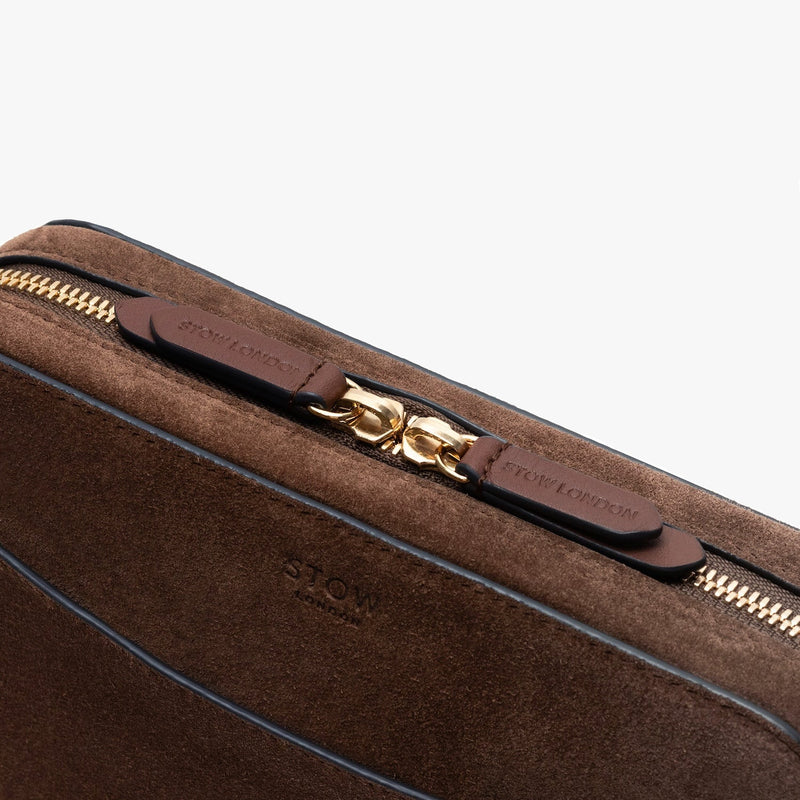 Close up of STOW London's Camera bag in Chocolate Suede leather featuring gold-coated stainless steel hardware and blind embossed logos on a light grey background