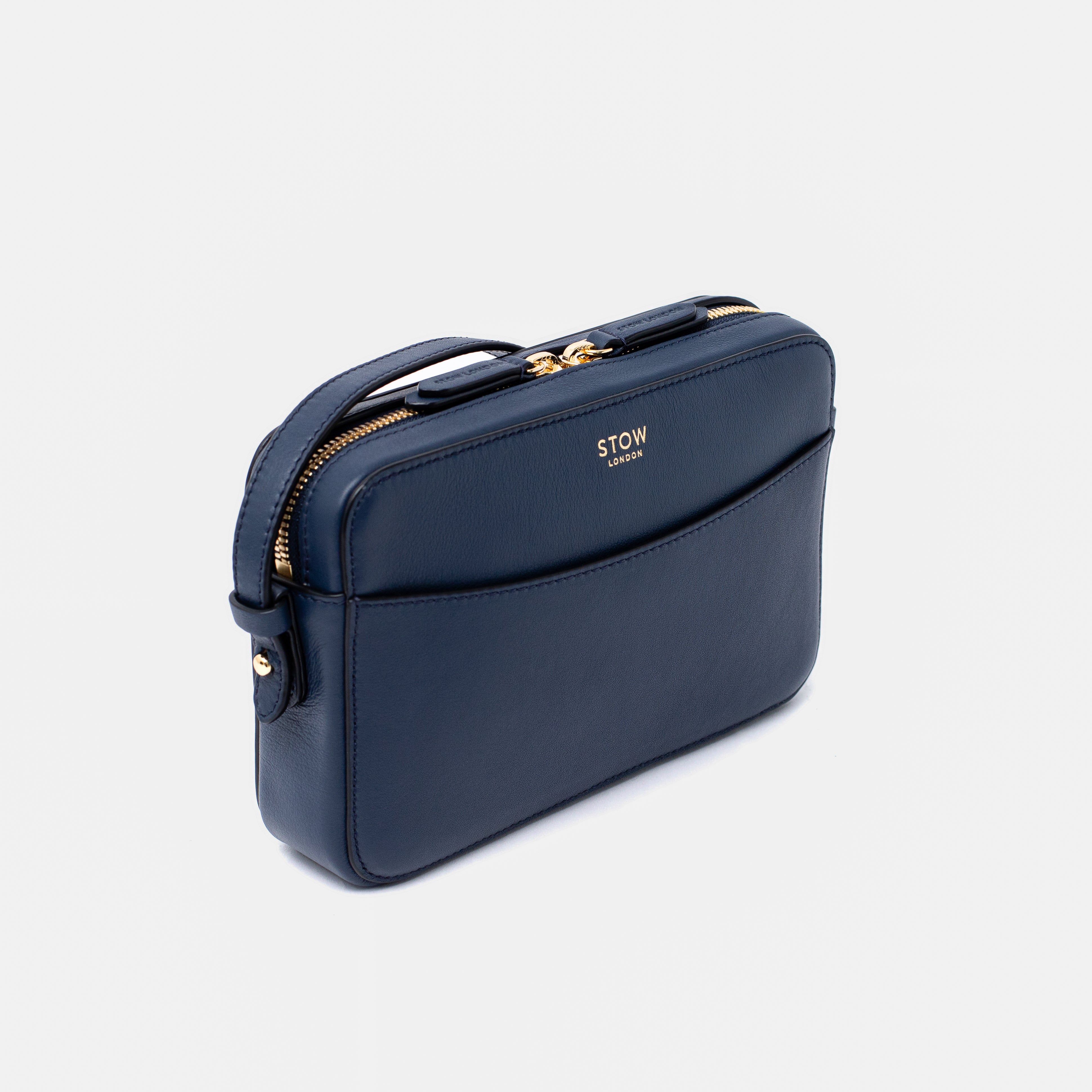 Off-axis view of STOW London's Camera bag in Navy Smooth leather featuring gold-coated stainless steel hardware on a white background
