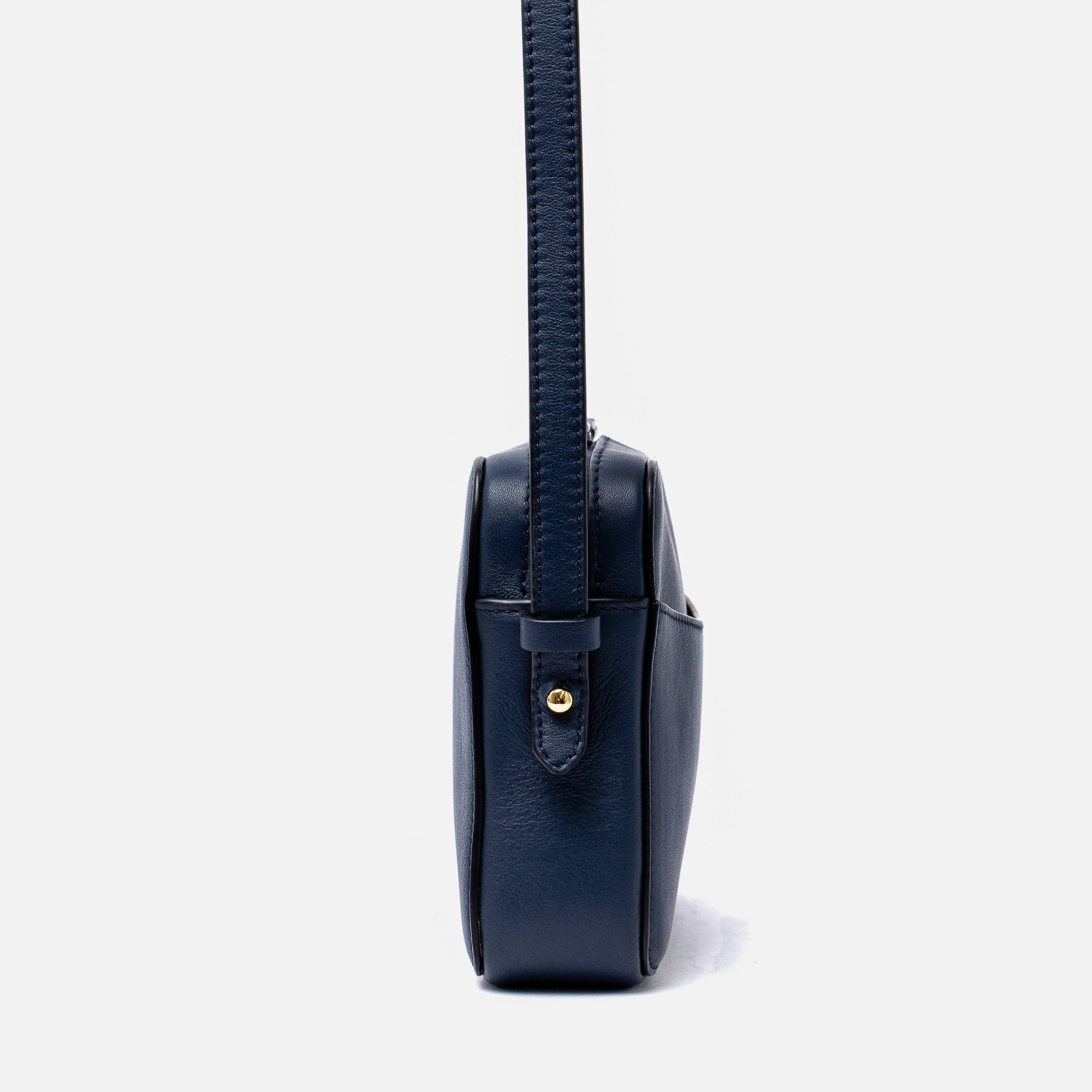 Side view of STOW London's Camera bag in Navy Smooth leather featuring gold-coated stainless steel hardware on a white background