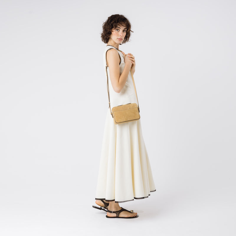 Model wearing STOW London's Camera bag in Soft Sand Suede leather on her shoulder with adjustable strap featuring gold-coated stainless steel hardware on a white background