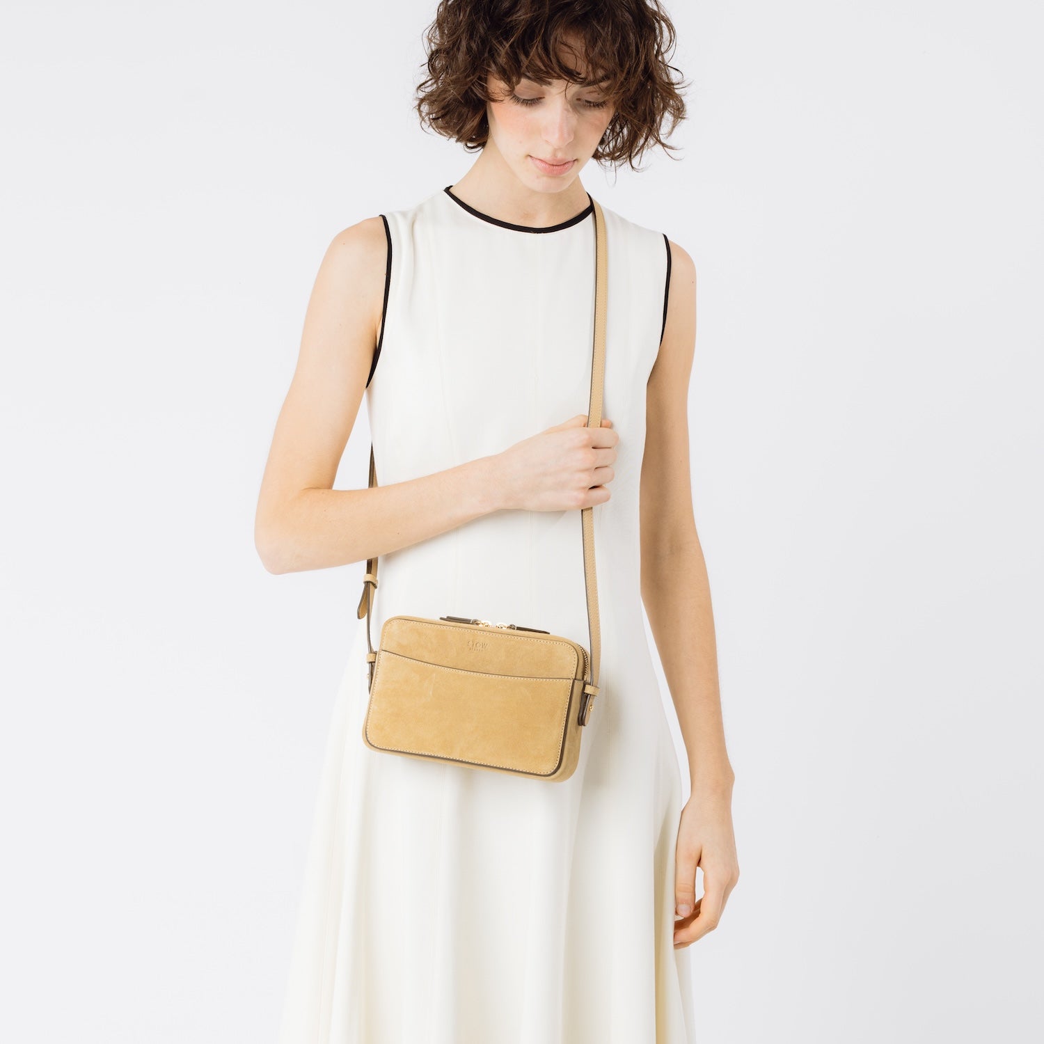 Model wearing STOW London's Camera bag in Soft Sand Suede leather crossbody with detachable strap featuring gold-coated stainless steel hardware on a white background