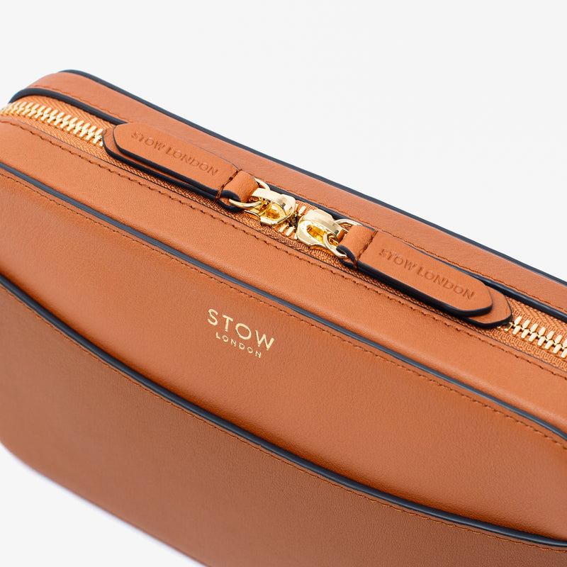 Close up of STOW London's Camera bag in Earth Tan Smooth leather featuring gold-coated stainless steel hardware and brand engraved pull tabs on a white background	