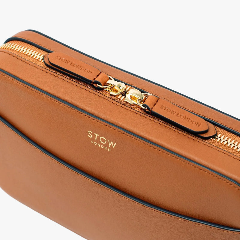 Close up of the top of STOW London's Camera bag in Earth Tan pebbled leather featuring the zip closure and gold-coated stainless steel hardware on a light grey background 