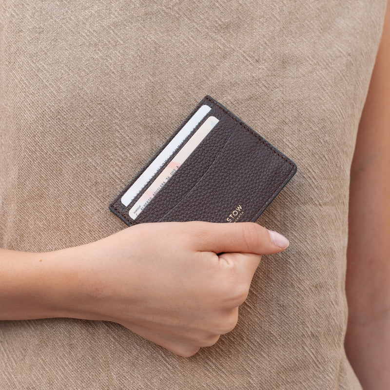 Model holding STOW London's Cardholder in Espresso pebbled leather featuring two cards and a small gold embossed logo on the front 