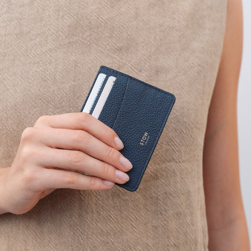 Model holding STOW London's Cardholder in Navy pebbled leather featuring two cards and a small gold embossed logo on the front 