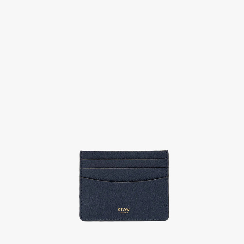 STOW London's Cardholder in Navy pebbled leather on a light grey background featuring a fine gold embossed logo on the front bottom. 