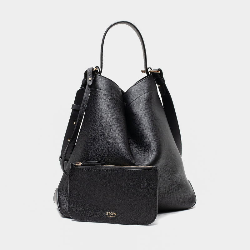 STOW London's Curve bag and matching, detachable interior pouch in Black leather featuring gold-coated stainless steel hardware on a light grey background
