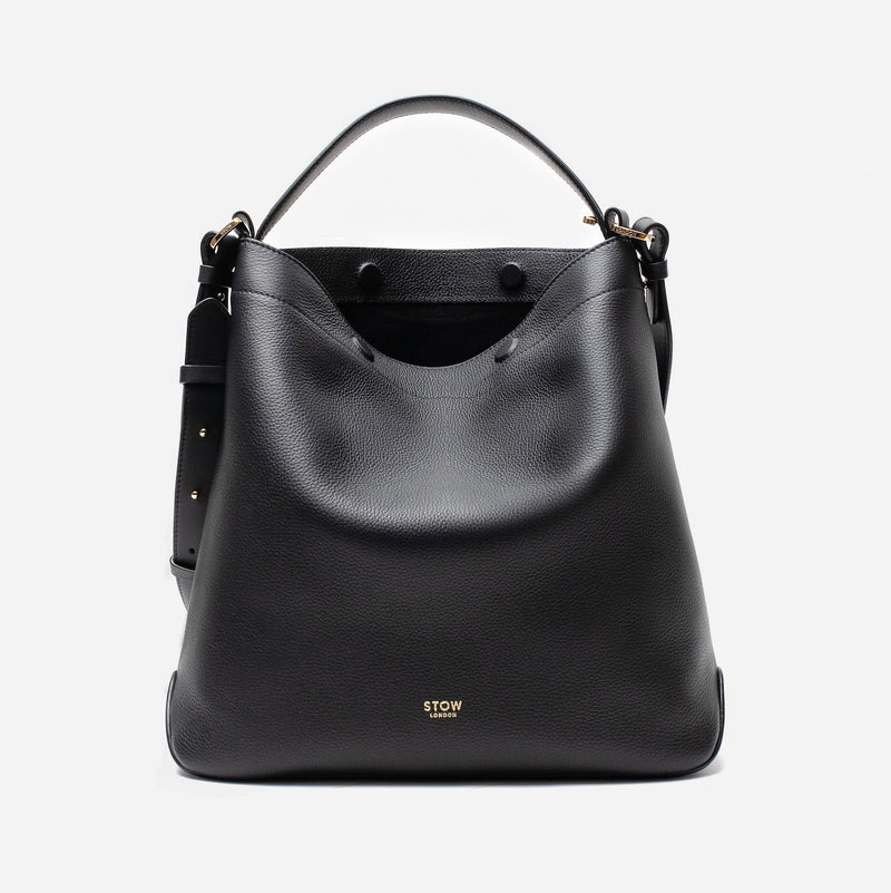STOW London's Curve bag in Black pebbled leather with magnets open showing the black suede interior lining featuring gold-coated stainless steel hardware on a light grey background