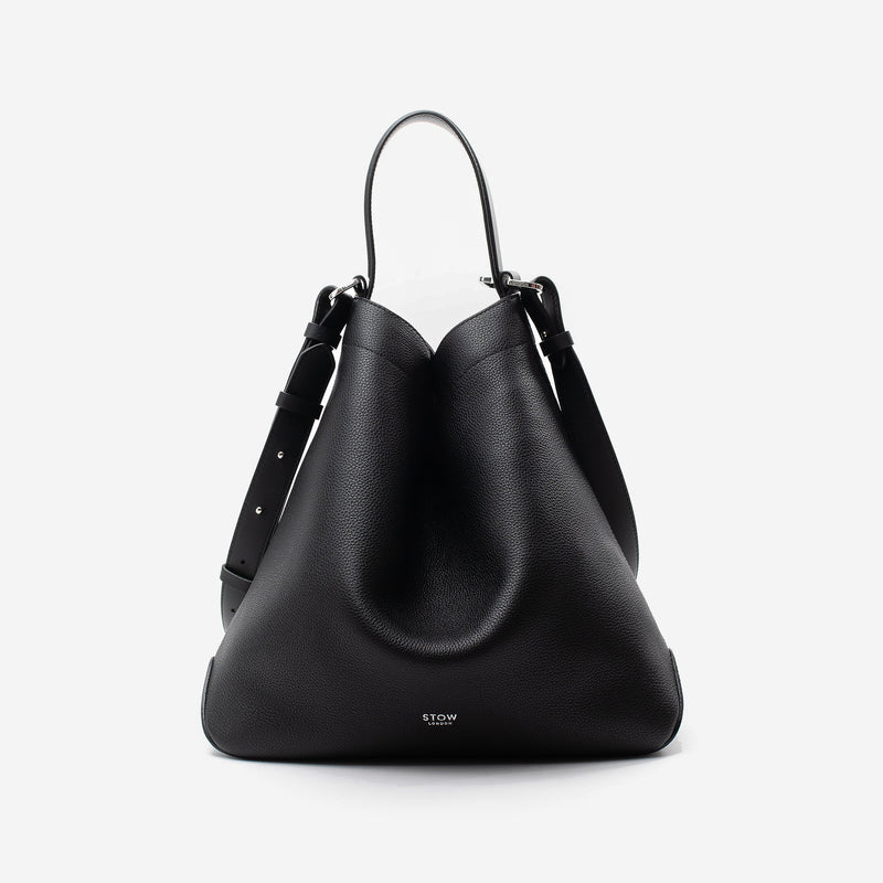 STOW London's Curve bag in Black pebbled leather shaped in a triangular featuring silver stainless steel hardware on a light grey background