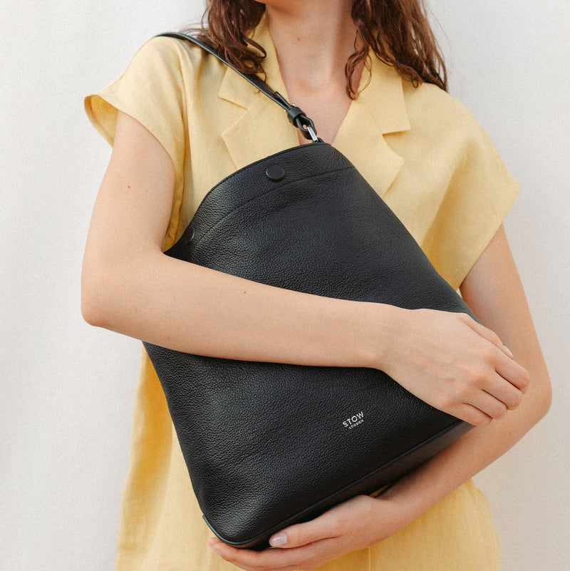 Model holding STOW London's Curve in Black leather featuring the detachable shoulder strap with silver hardware and details 