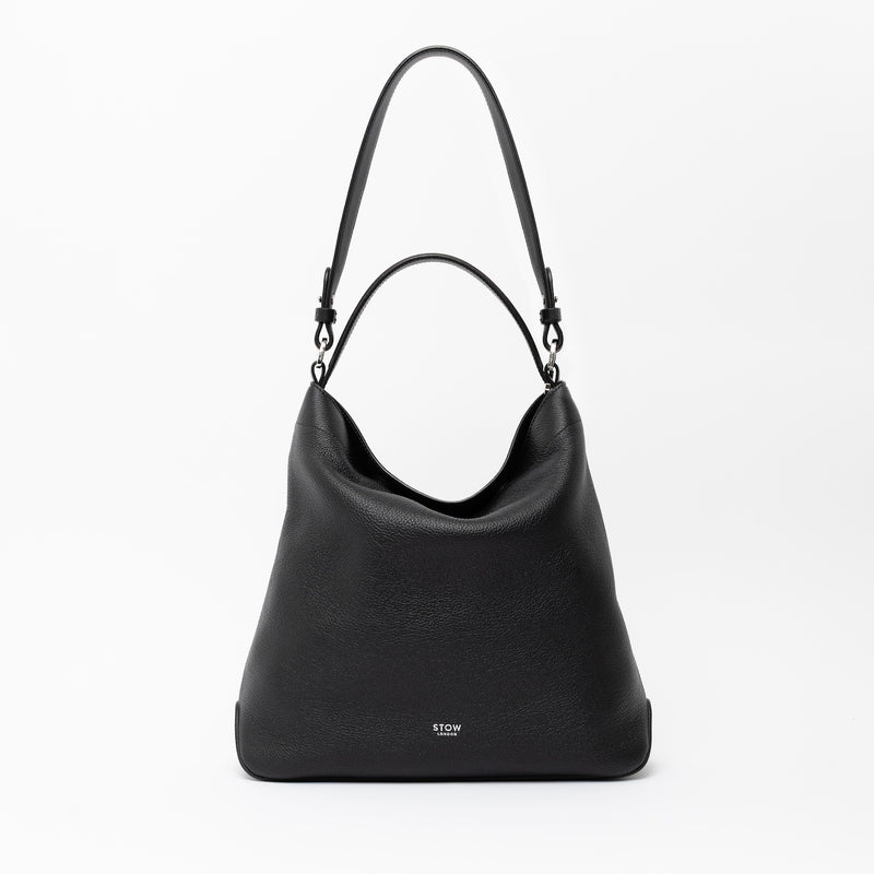 STOW London's Curve in Black leather on a light grey background featuring the detachable shoulder strap and its top handle with silver hardware and details 