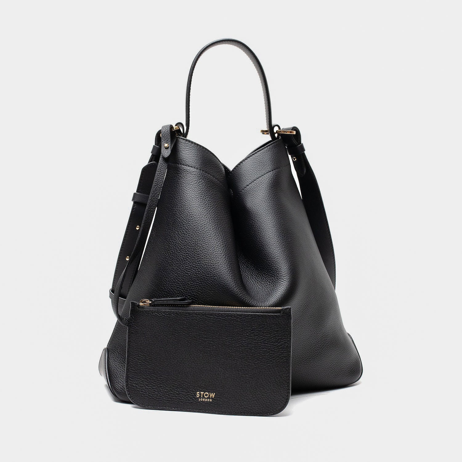 Stow London's Curve bag and matching, detachable interior pouch in Black pebbled leather featuring gold-coated stainless steel hardware on a light grey background