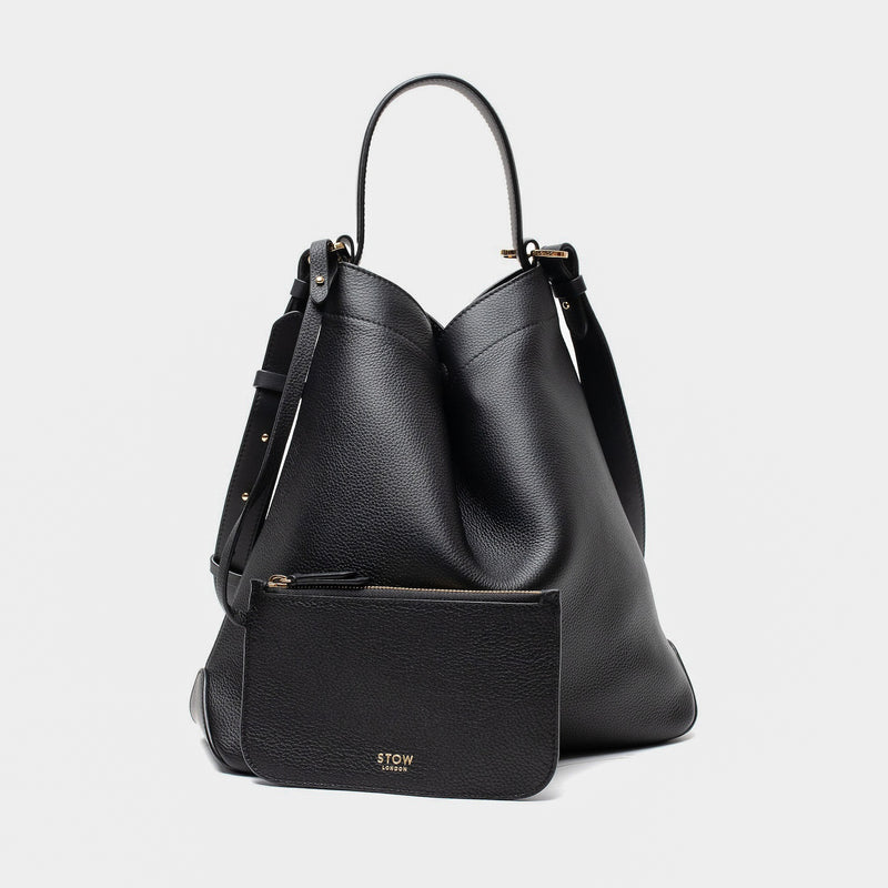 Stow London's Curve bag and matching, detachable interior pouch in Black pebbled leather featuring gold-coated stainless steel hardware on a light grey background