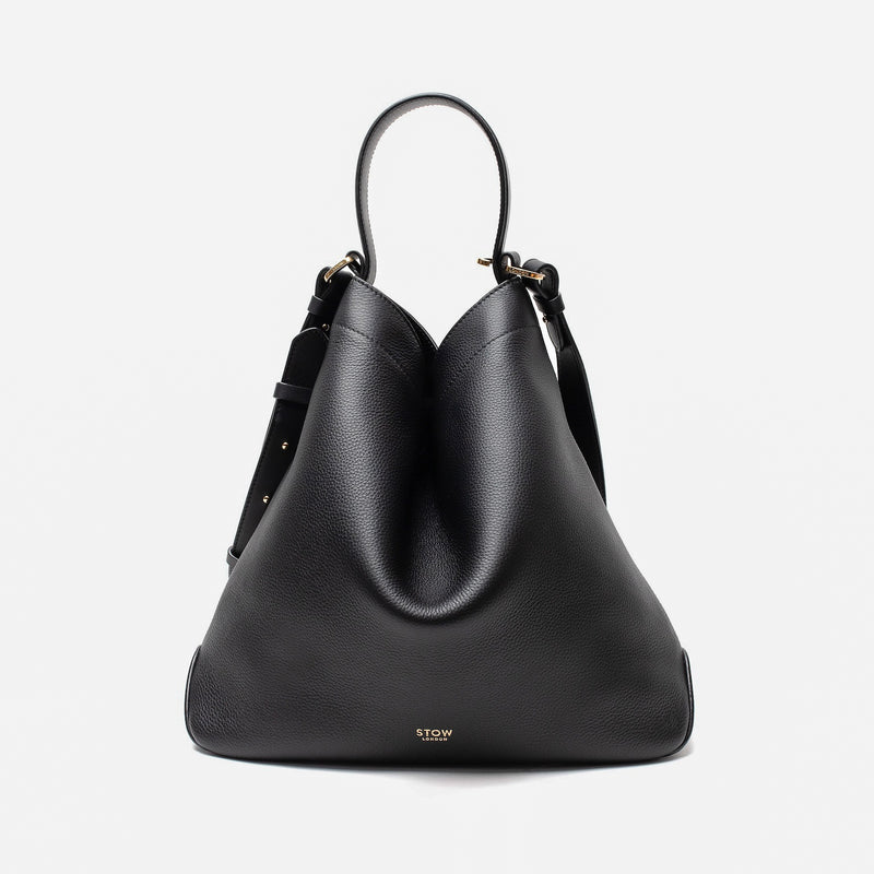 Stow London's Curve bag in Black pebbled leather shaped in a triangular form featuring gold-coated stainless steel hardware on a light grey background