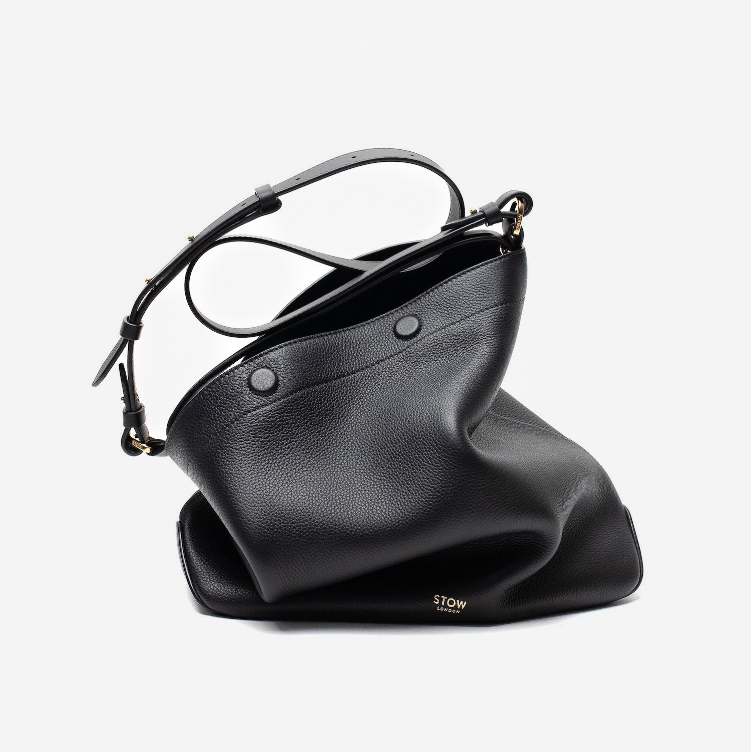 Stow London's Curve bag in Black pebbled leather featuring gold-coated stainless steel hardware on a light grey background