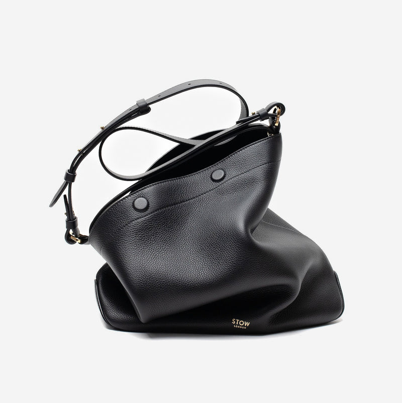 Stow London's Curve bag in Black pebbled leather featuring gold-coated stainless steel hardware on a light grey background