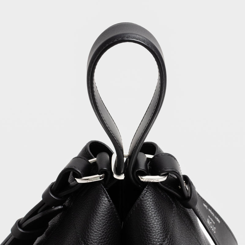 Close up of the handles on Stow London's Curve bag in Black pebbled leather featuring silver stainless steel hardware and clip and detachable strap on a light grey background