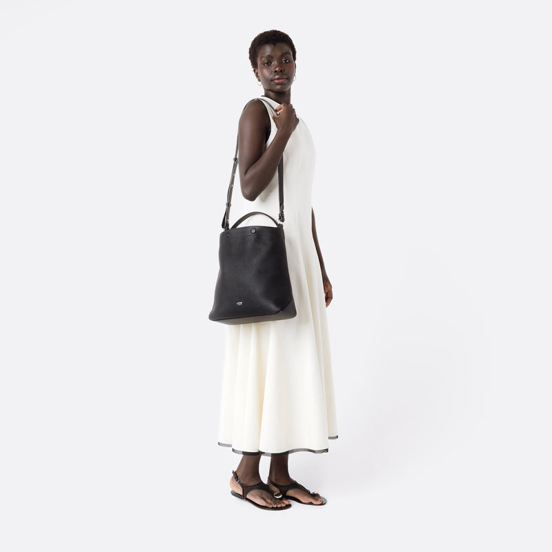 Model wearing Stow London's Curve bag in Black pebbled leather on her shoulder featuring silver stainless steel hardware on a light grey background
