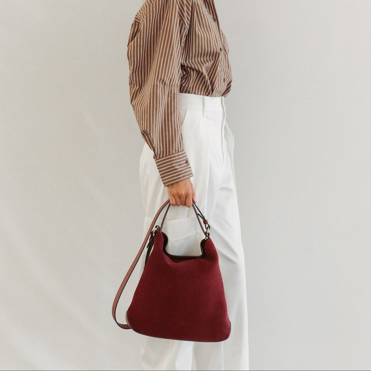 Model holding STOW London's Curve bag in Burgundy Suede leather featuring the detachable crossbody strap