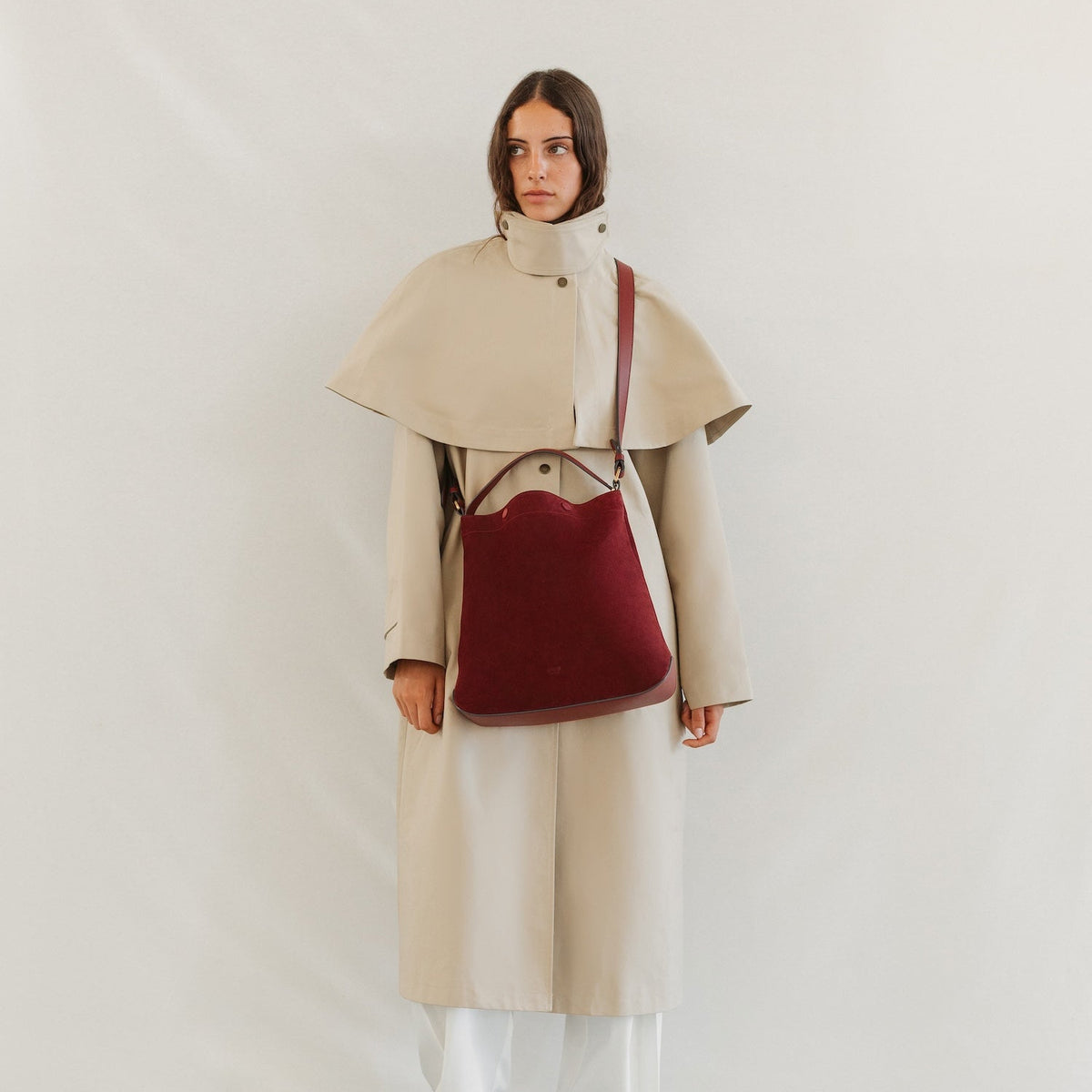 Model in a trench coat wearing STOW London's Curve bag in Burgundy Suede leather crossbody