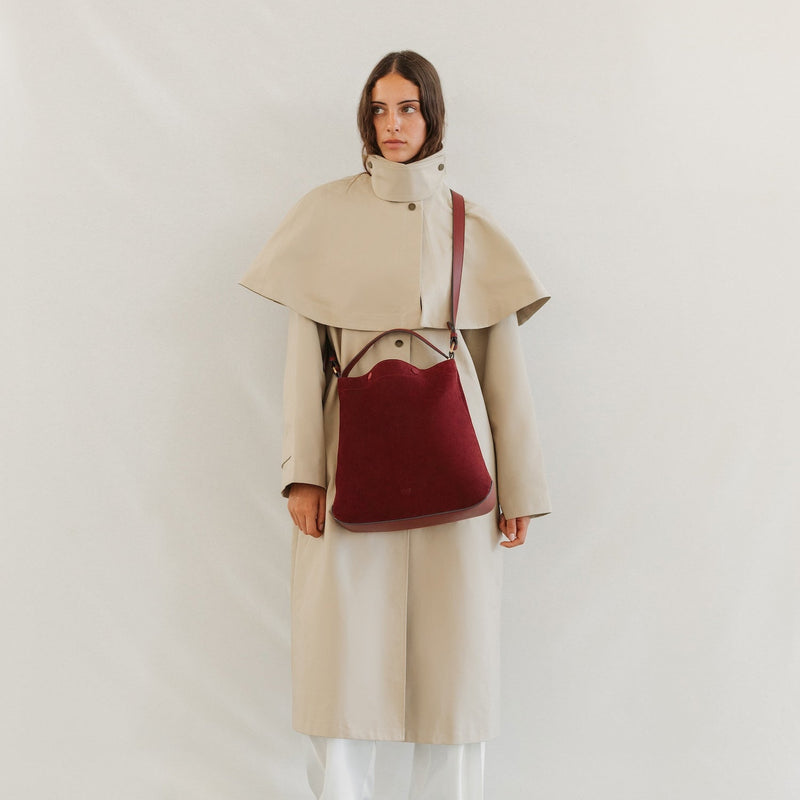 Model in a trench coat wearing STOW London's Curve bag in Burgundy Suede leather crossbody